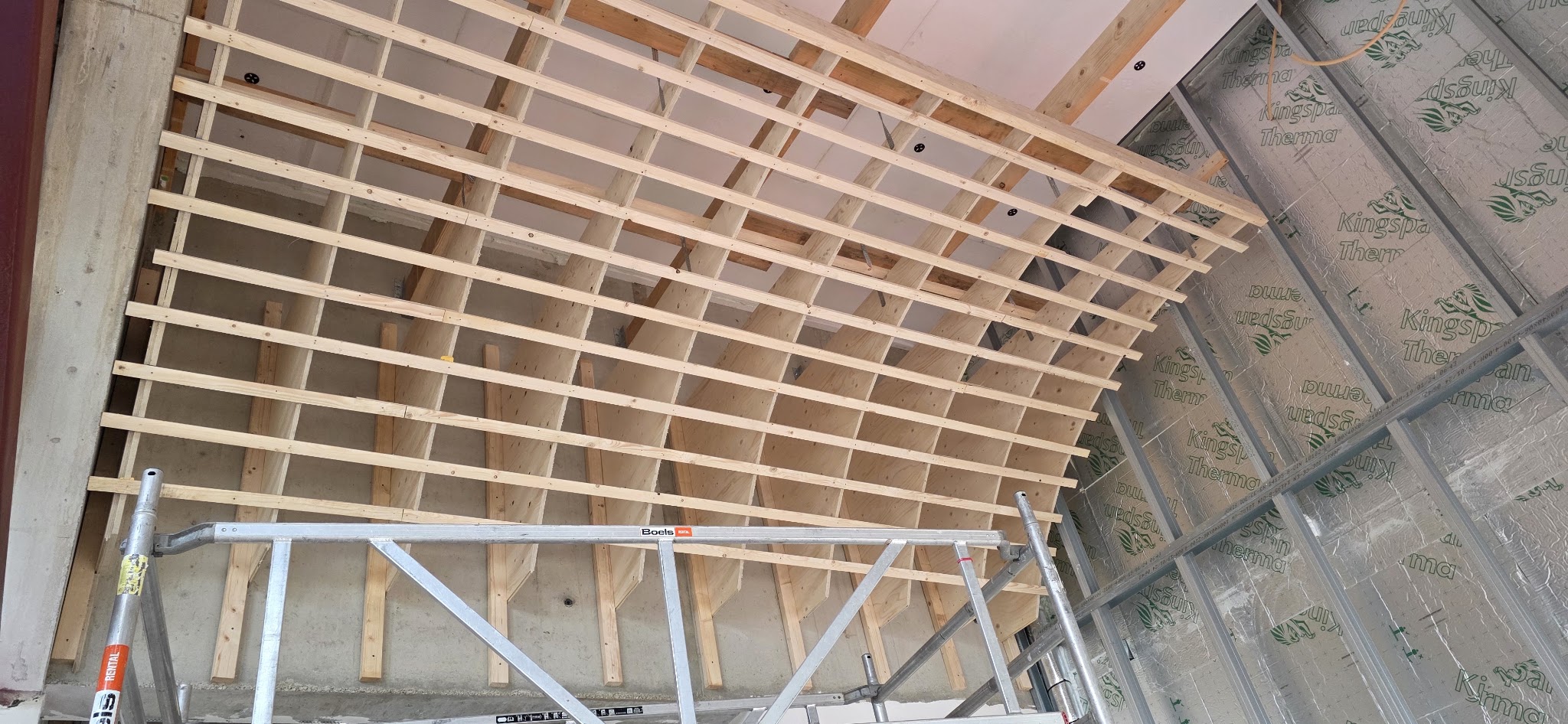 Houten regelwerk in een boog onder een betonnen plafond, met metalen profielen en isolatie aan de zijkant