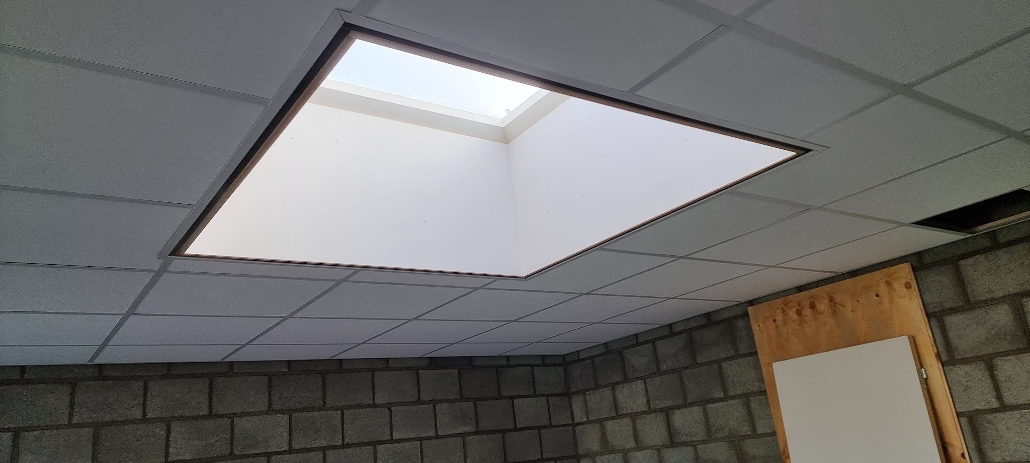 Wit systeemplafond met een vierkante lichtkoepel in een ruimte met betonblokken wanden