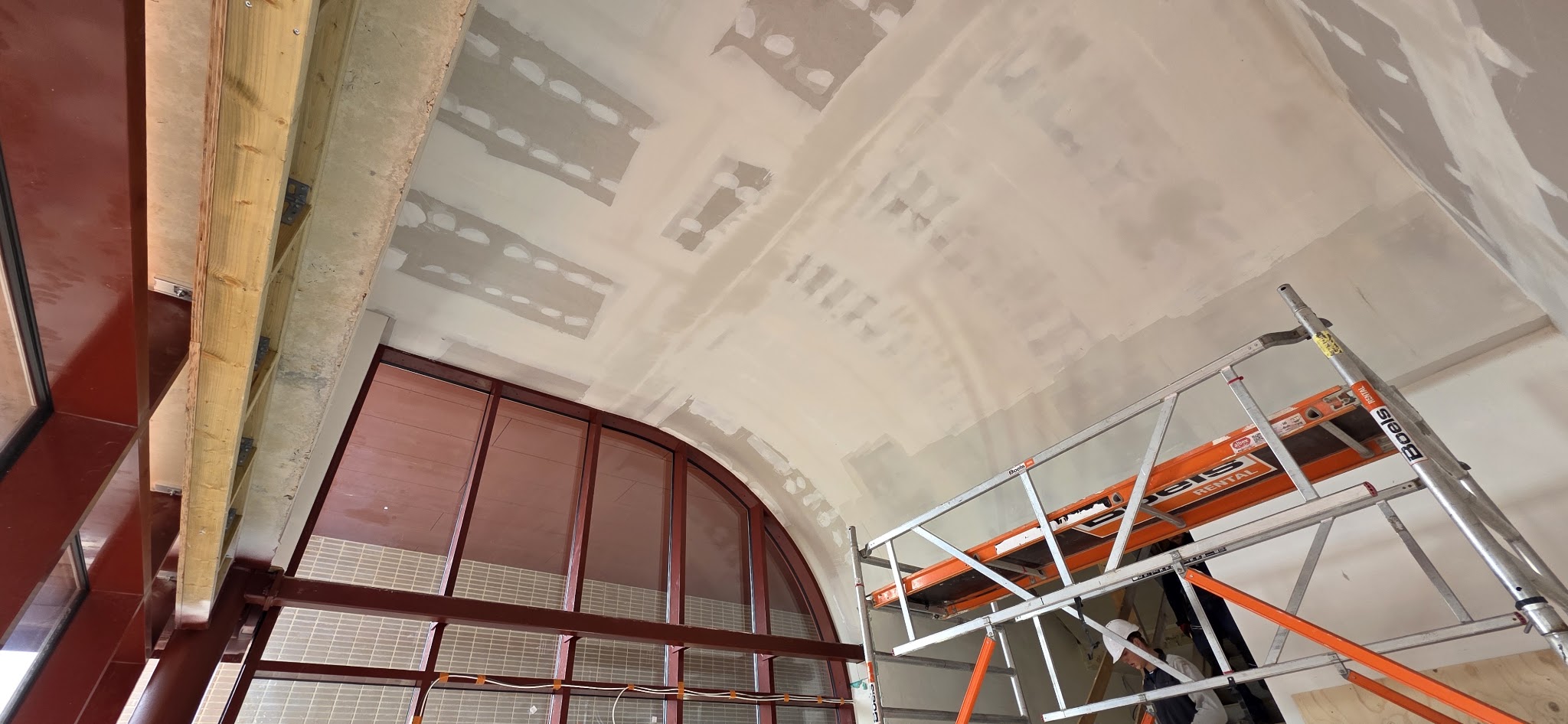 Gewelfd plafond met gevulde naden boven een groot boogvormig raam, met een rolsteiger